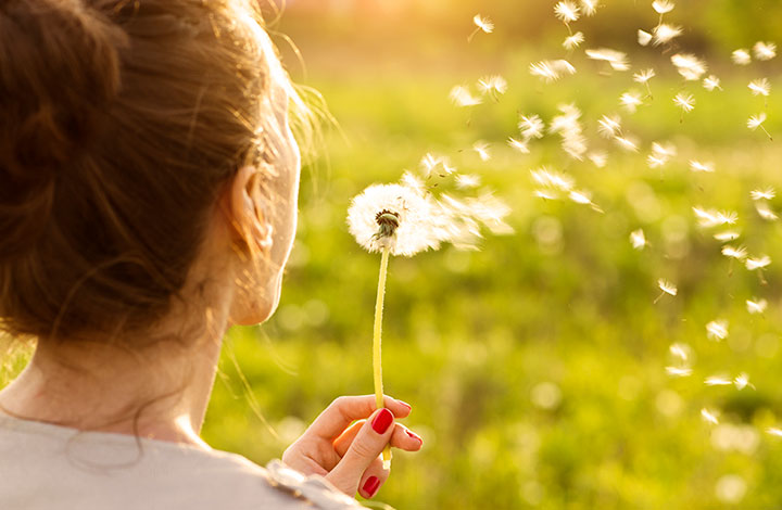 Frau pustet eine Blume.
